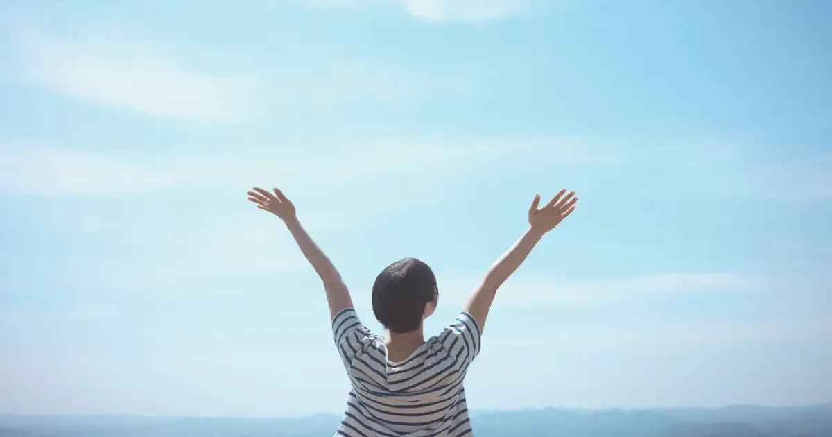Woman who has found freedom and healing after loss celebrating with her hands up in the air.
