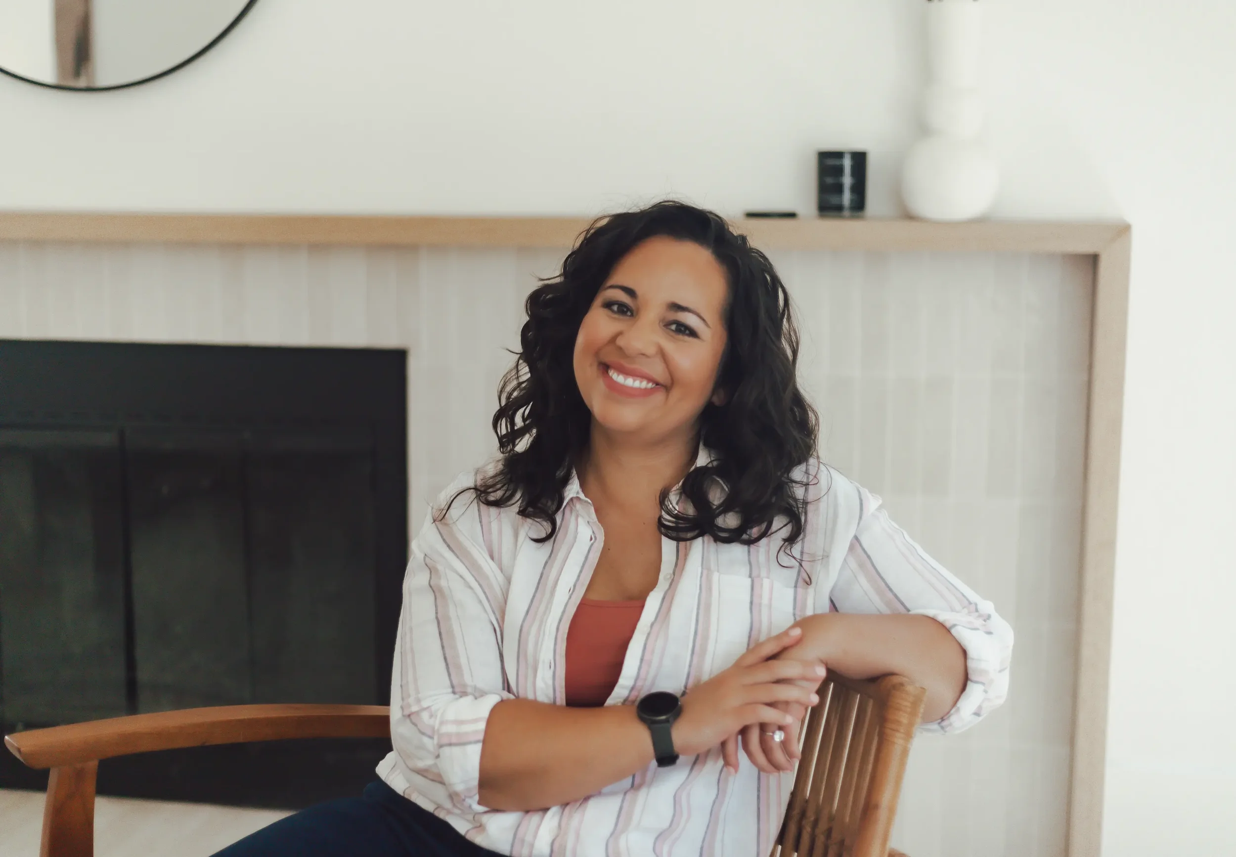 Gottman couples workshop facilitator with dark brown curly hair wearing a white striped button up shirt while sitting on a wooden chair.