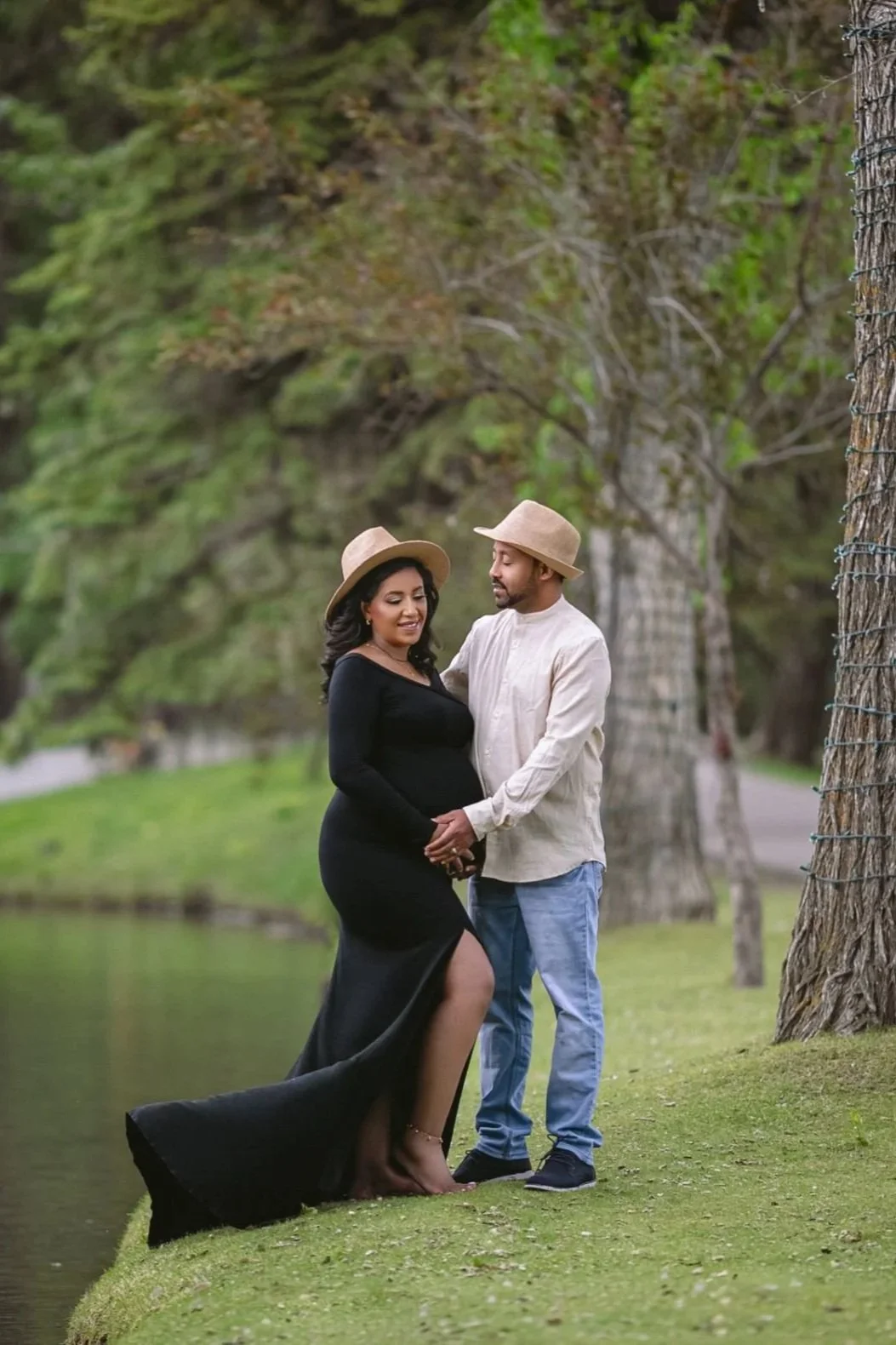 A pregnant woman standing with a man in a maternity photoshoot, wearing a black bodycon dress