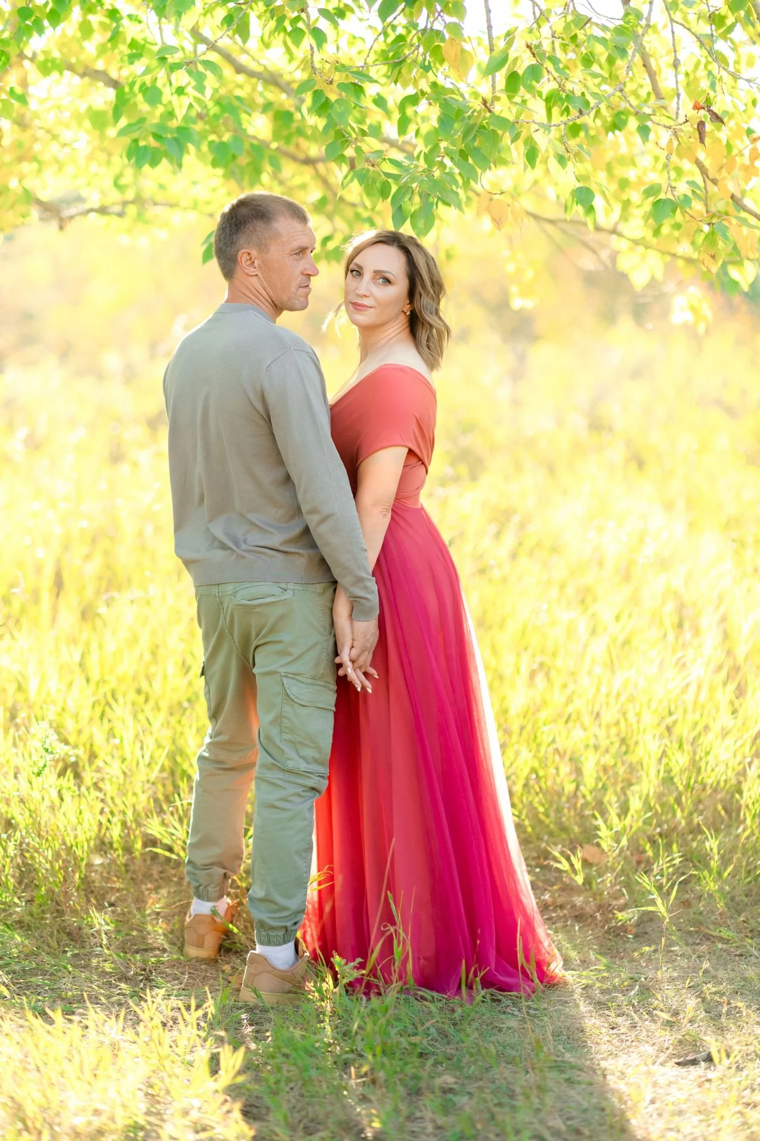 A woman wearing a bright peach coloured dress with a tulle skirt, standing next to a man in a Calgary outdoor family photoshoot