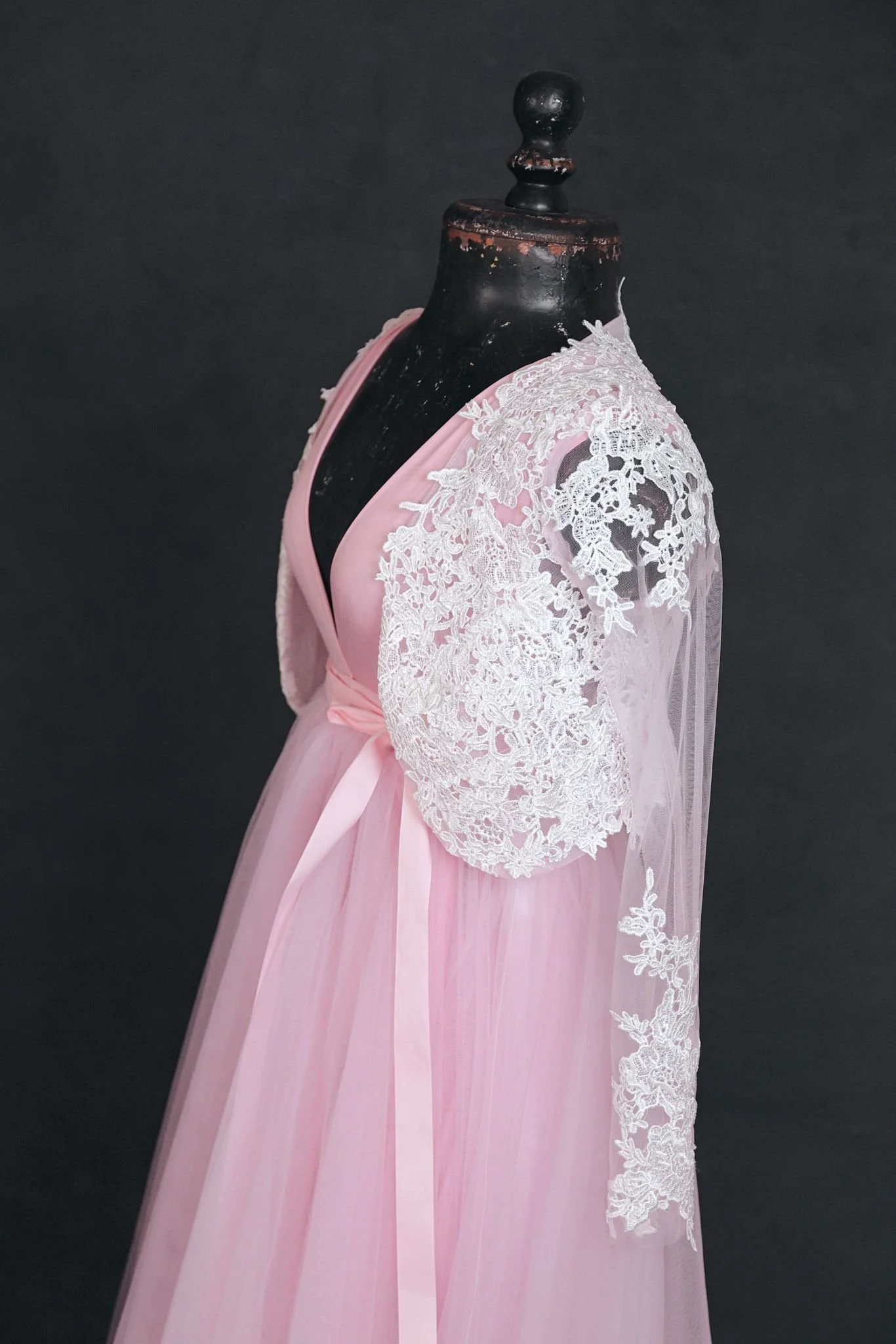 Side view of pink infinity dress with a tulle skirt and white lace coat added overtop, tied with a pink ribbon at the waist