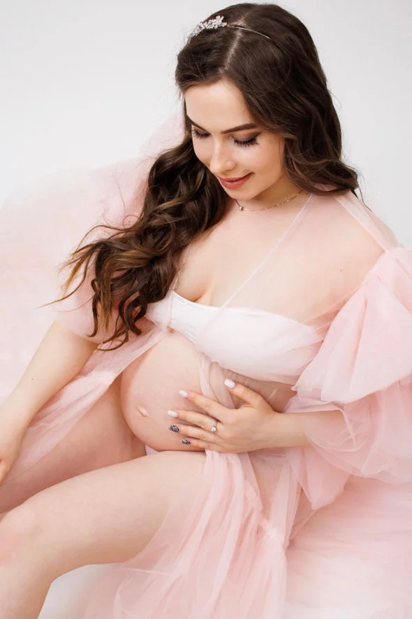 Pregnant woman posing in a maternity photoshoot wearing a light pink fluffy tulle robe