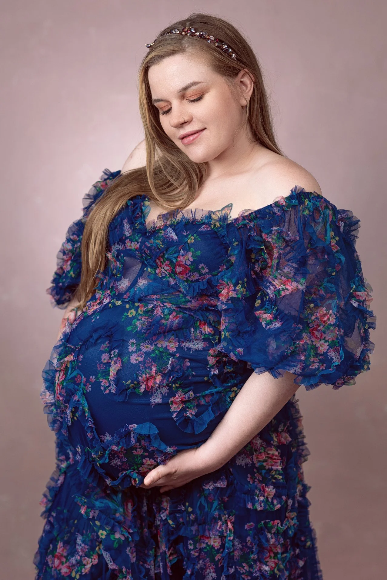 Close up of pregnant woman wearing a navy blue dress with floral patterns and a lot of tulle texture, a maxi mermaid skirt, and off-the-shoulder sheer sleeves