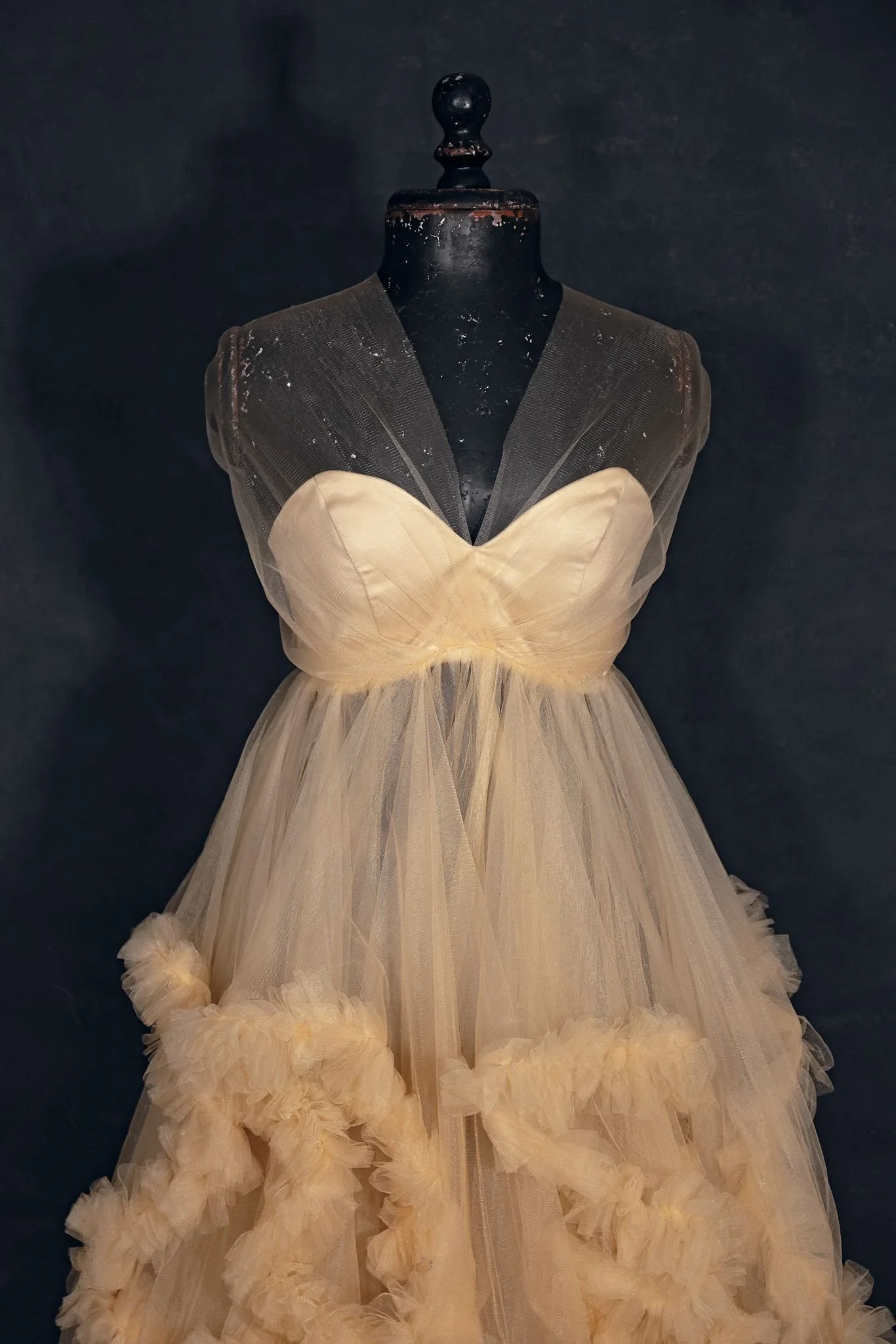 Closeup of a puffy tulle beige coloured gown on a mannequin. The skirt is layered tulle and the gown is shoulderless.