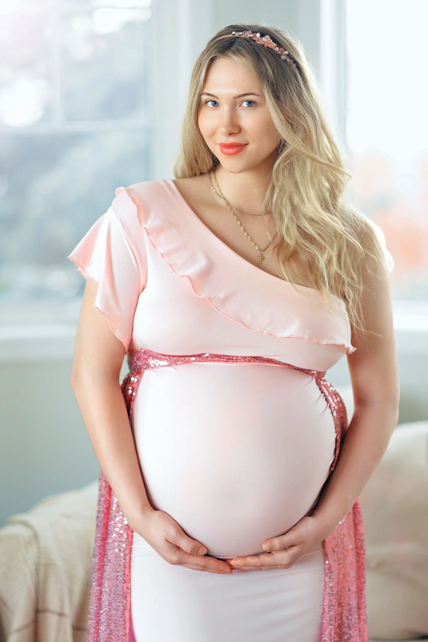 A pregnant woman wearing a barbie pink one shoulder dress with a sparkly sequin skirt