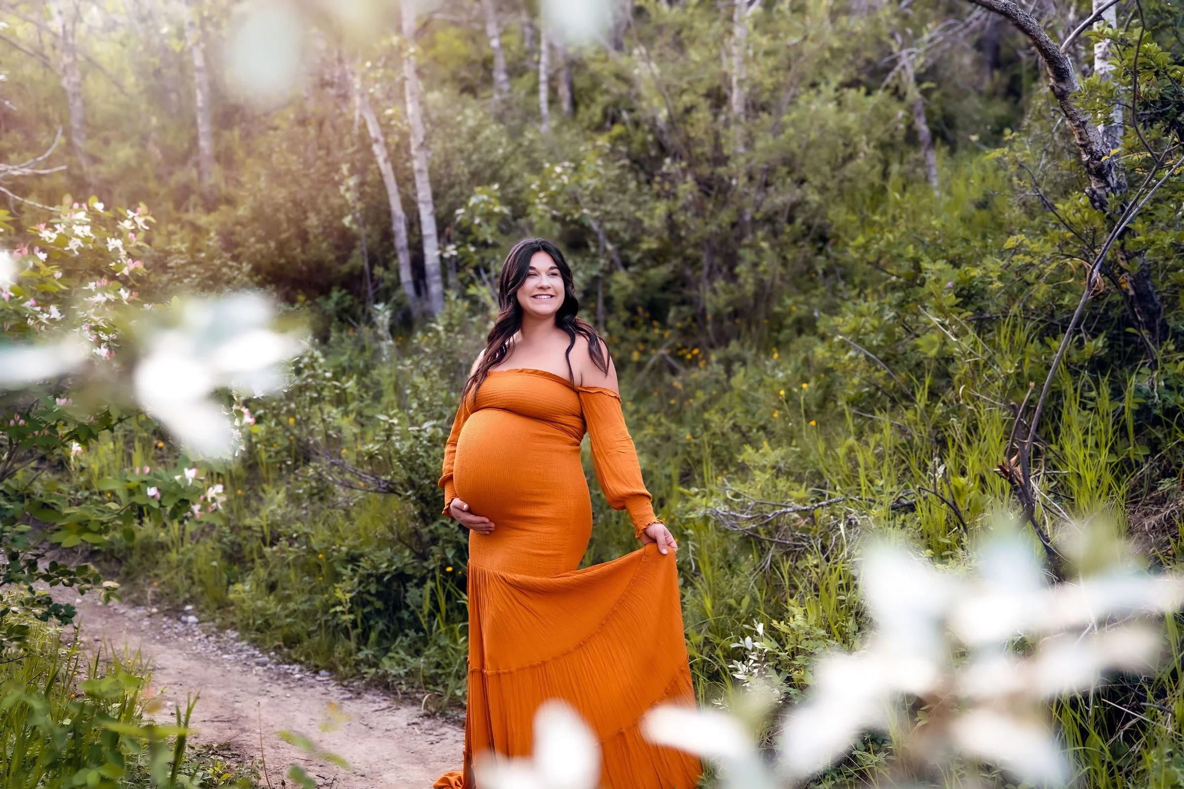 A pregnant woman wearing a strapless orange boho mermaid dress in outdoor maternity photoshoot in Calgary