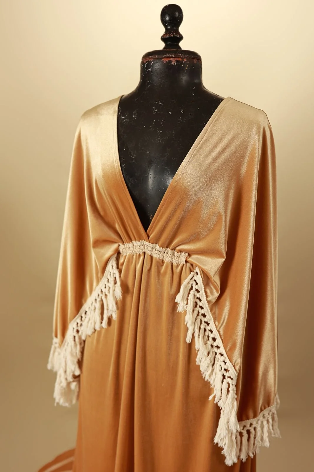 Close up of a golden yellow velvet gown with v-neck, open back, and long boho tassled sleeves
