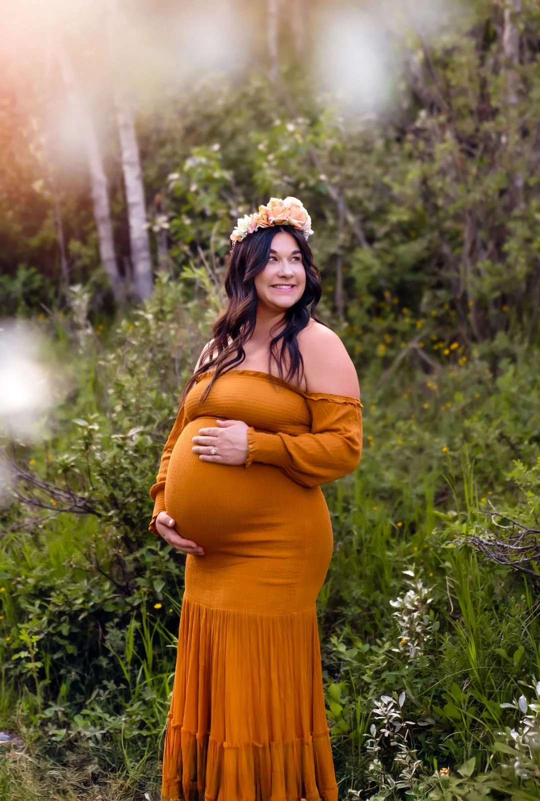 A pregnant woman wearing a flower crown and strapless orange boho mermaid dress in outdoor maternity photoshoot in Calgary,