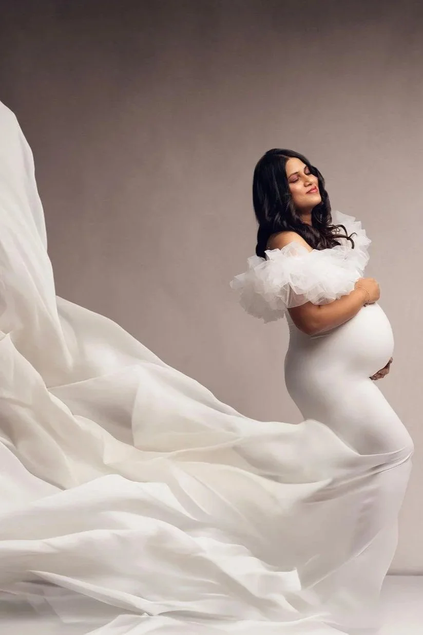 A pregnant woman wearing a white bodycon gown in a studio photoshoot in Calgary