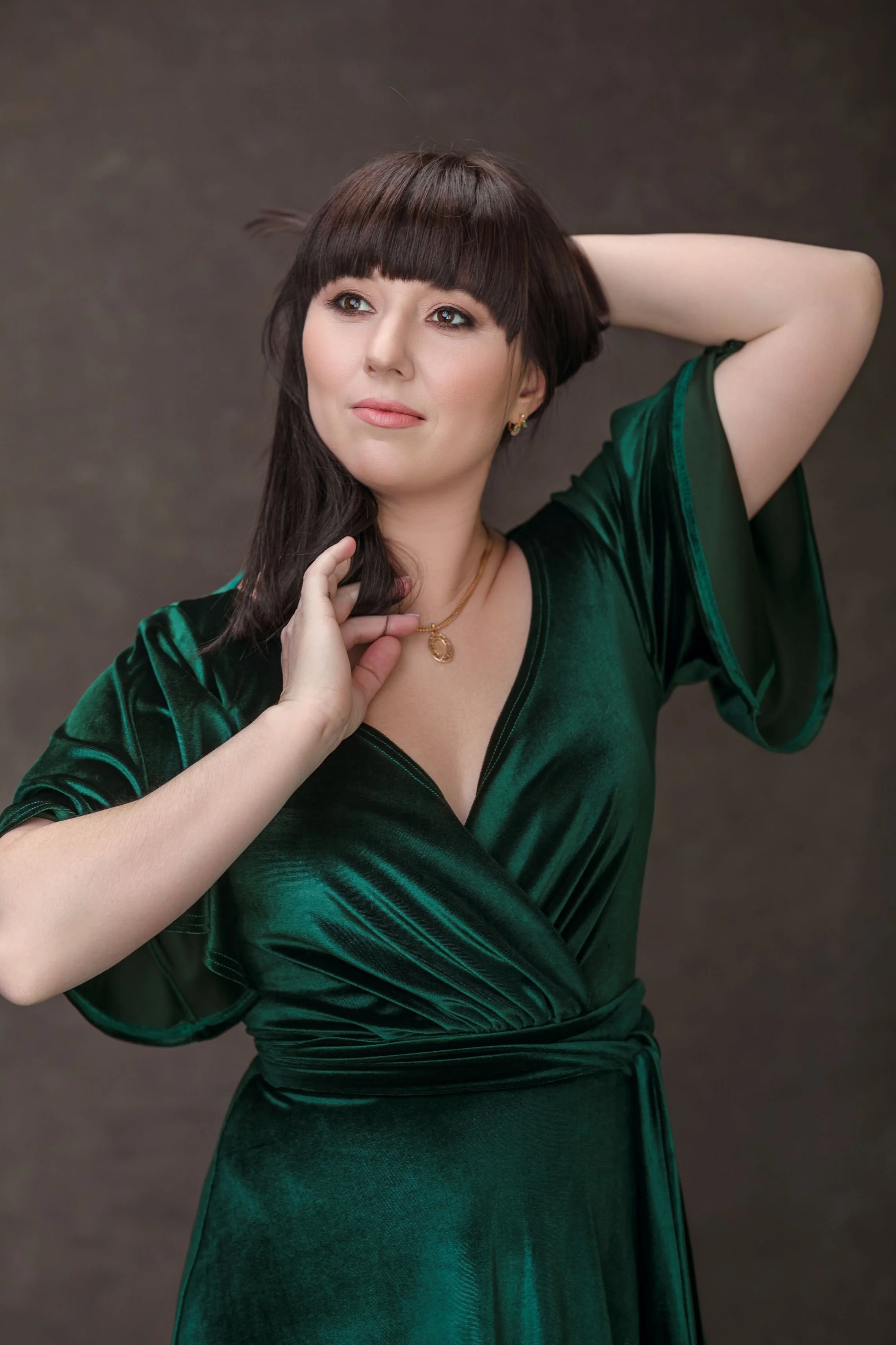 Woman in a green velvet V-neck dress, posing in an indoor studio photoshoot in Calgary