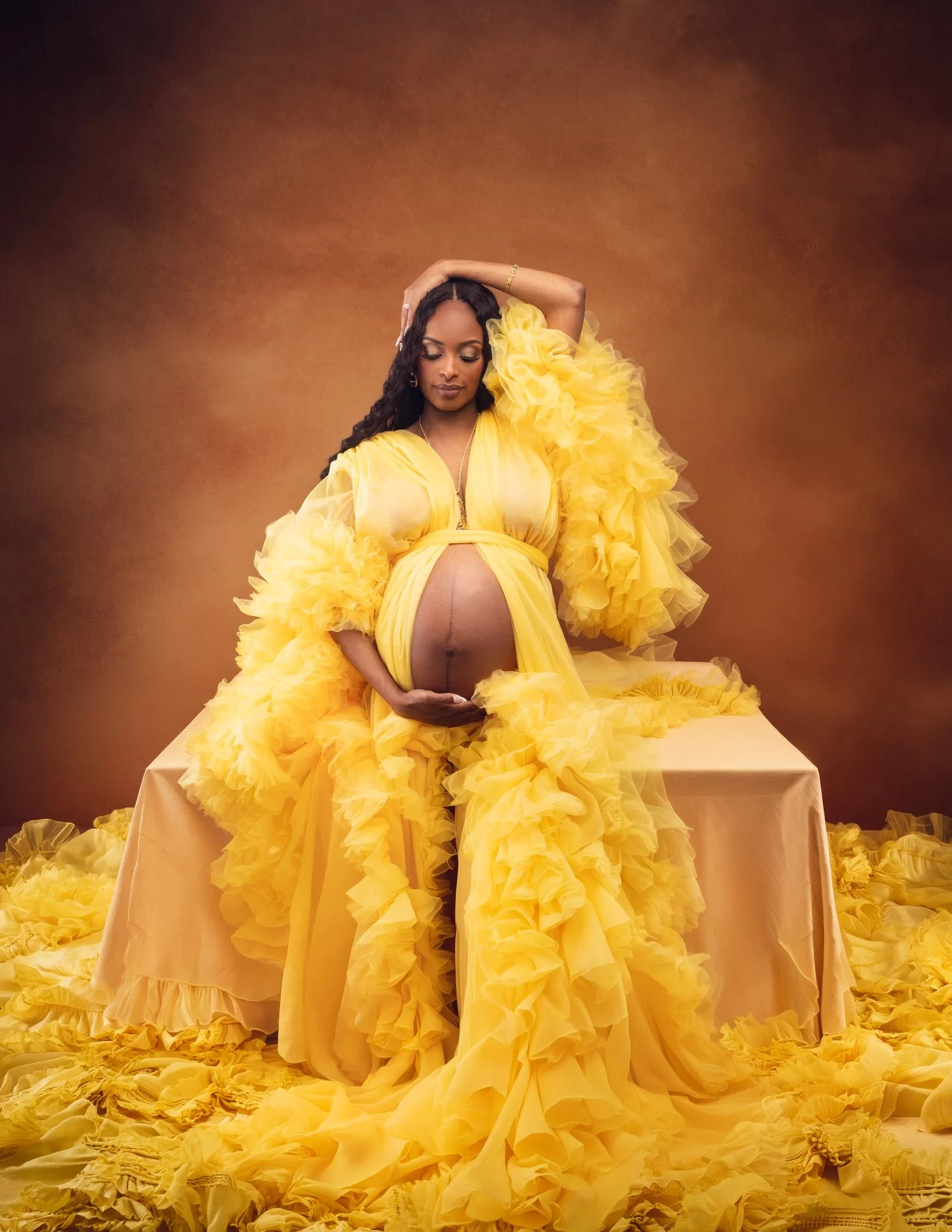 A pregnant woman wearing a golden yellow sheer tulle maternity robe with open belly front, posing in a studio pregnancy photoshoot