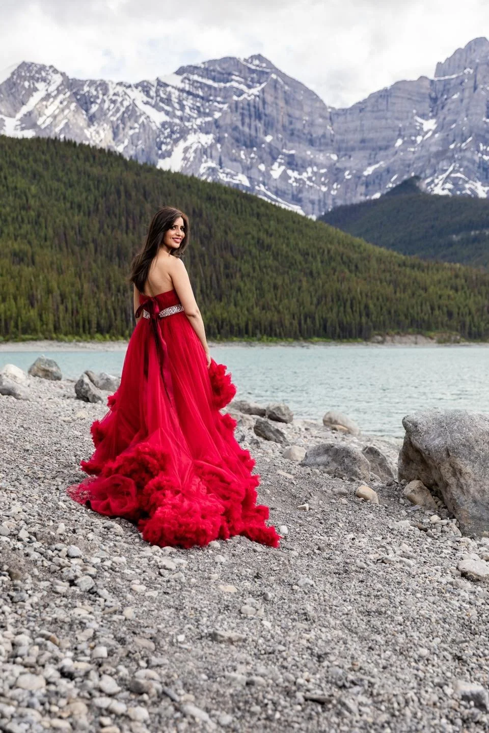 A woman wearing a red gown, standing in the mountains in an outdoor photoshoot in Calgary