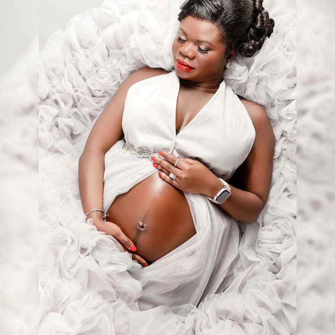 A pregnant woman laying down, wearing a white puffy sheer tulle gown in a studio maternity photoshoot setting