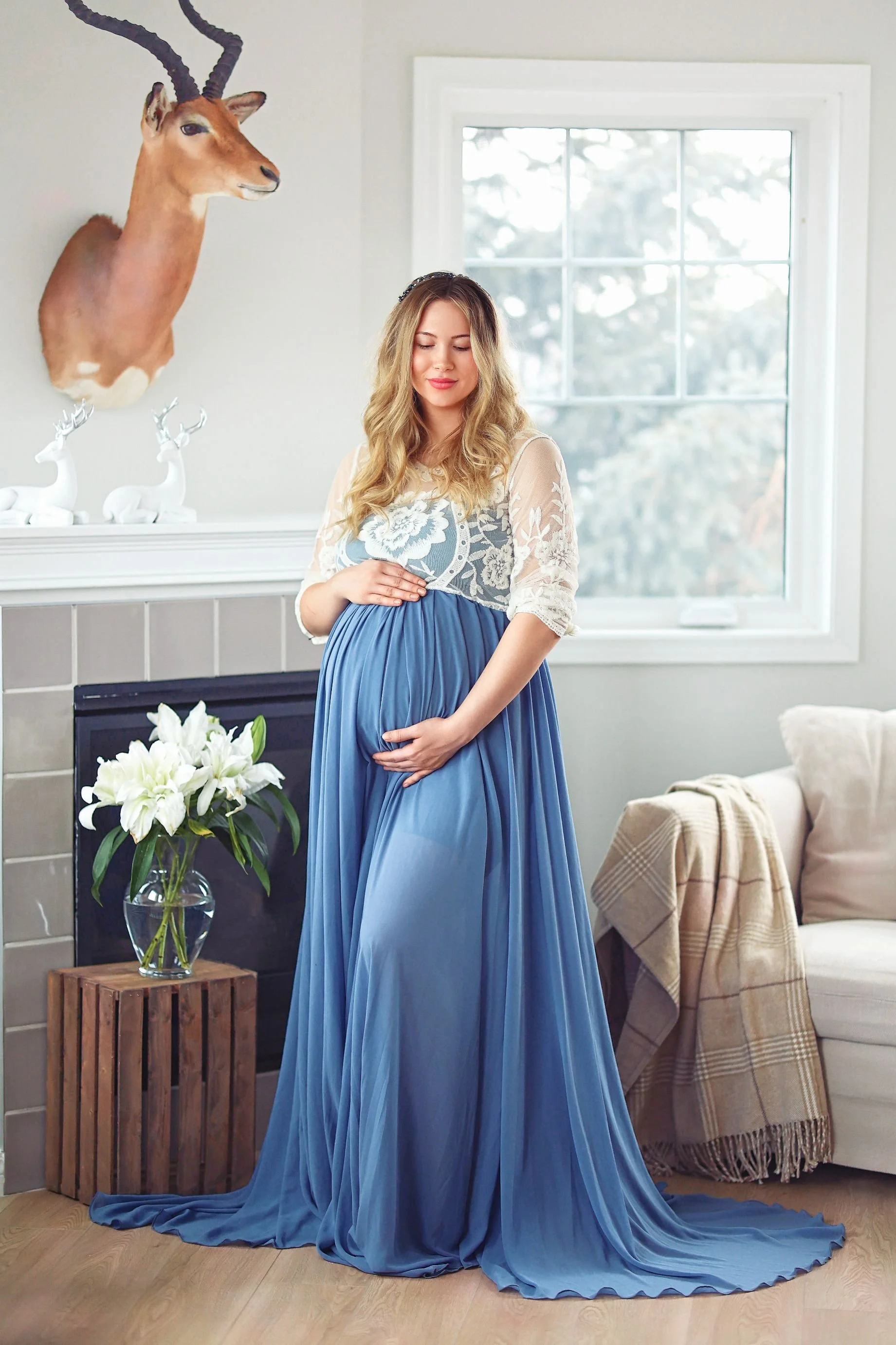 A pregnant woman wearing a blue maternity rental dress with a white lace embroidered top