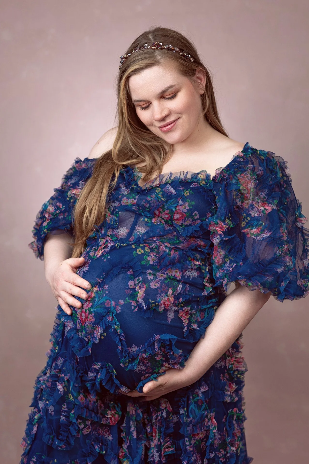Close up of pregnant woman wearing a navy blue dress with floral patterns and a lot of tulle texture, a maxi mermaid skirt, and off-the-shoulder sheer sleeves