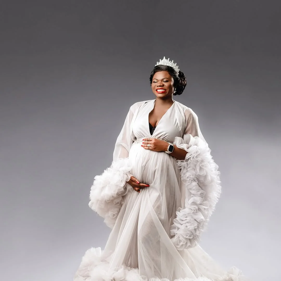 A pregnant woman wearing a white puffy sheer tulle gown in a studio maternity photoshoot setting