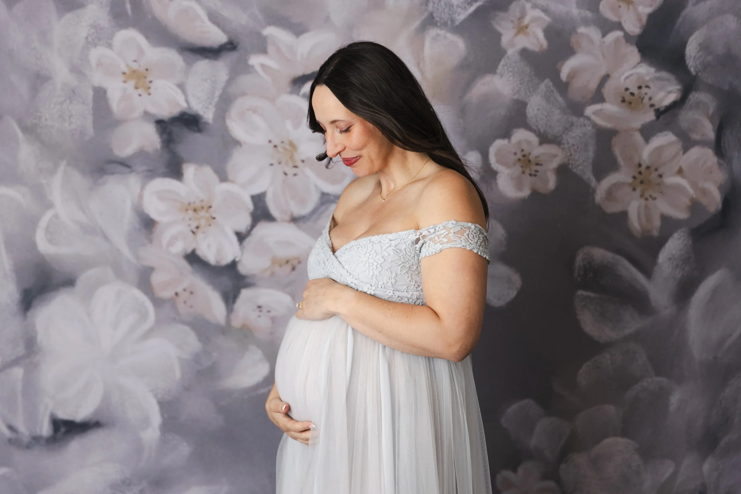 A pregnant woman wearing a silver tulle rental dress with off-the-shoulder embroidered corset, in a studio maternity photoshoot in Calgary