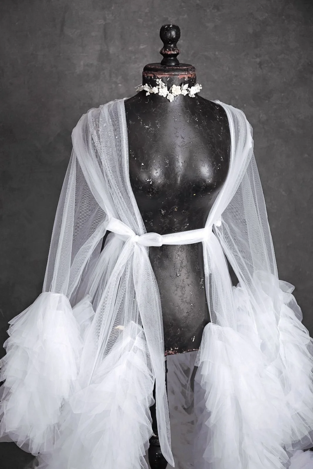 Close up of white sheer tulle floor-length robe with puffy textured sleeves, and jewellery ribbon