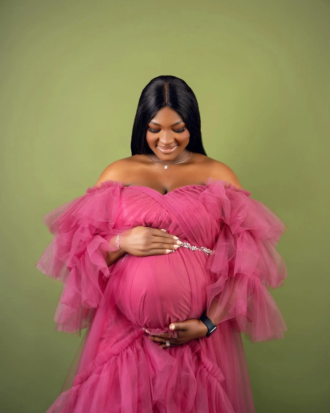 Close up of pregnant woman wearing a pink layered shoulderless tulle gown with silver jewellery belt
