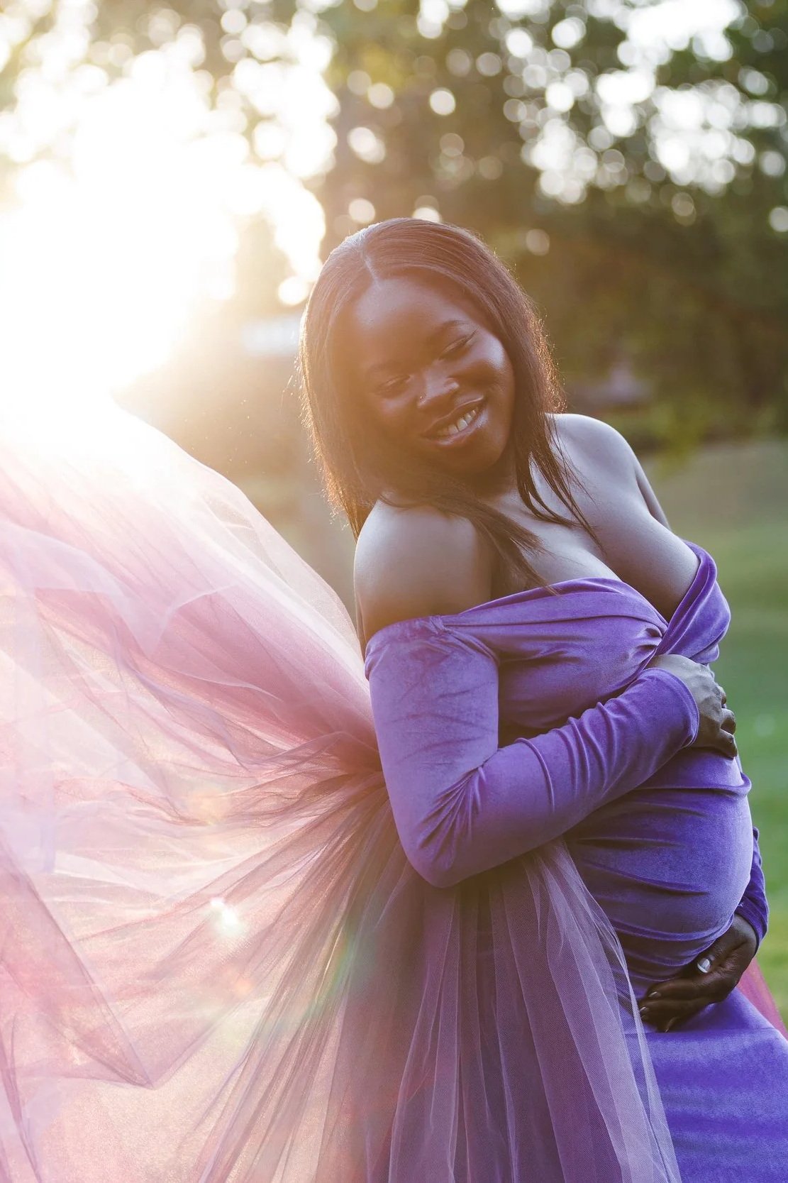 A pregnant lady wearing a purple velvet dress and light pink tulle tail in an outdoor Calgary maternity photoshoot