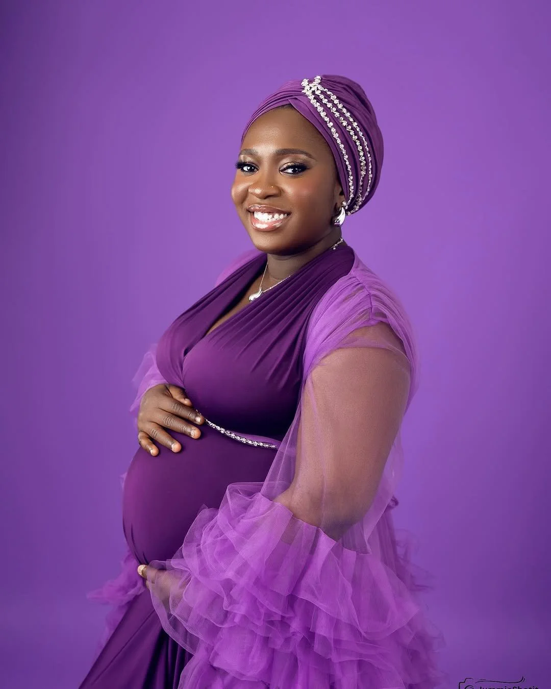 Close up of pregnant woman wearing a silky dark purple dress and fluffy tulle robe in studio maternity photoshoot