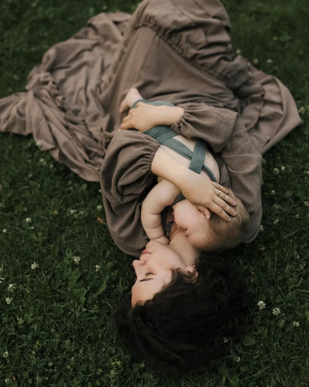 A woman wearing a khaki brown top and skirt, holding a newborn in an outdoor photoshoot setting in Calgary