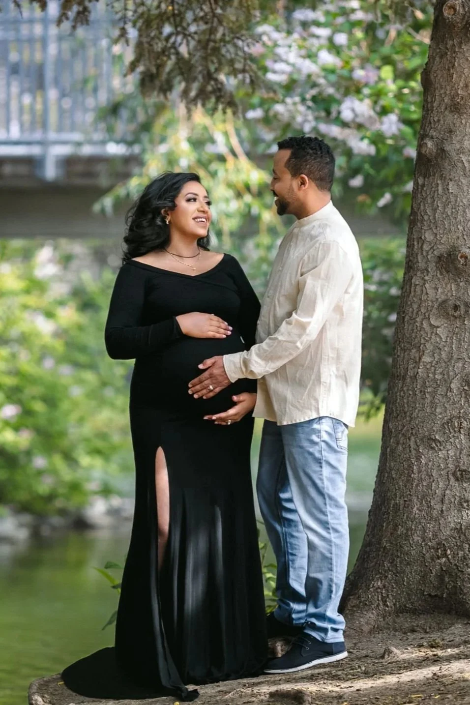 A pregnant woman standing with a man in a maternity photoshoot, wearing a black bodycon dress