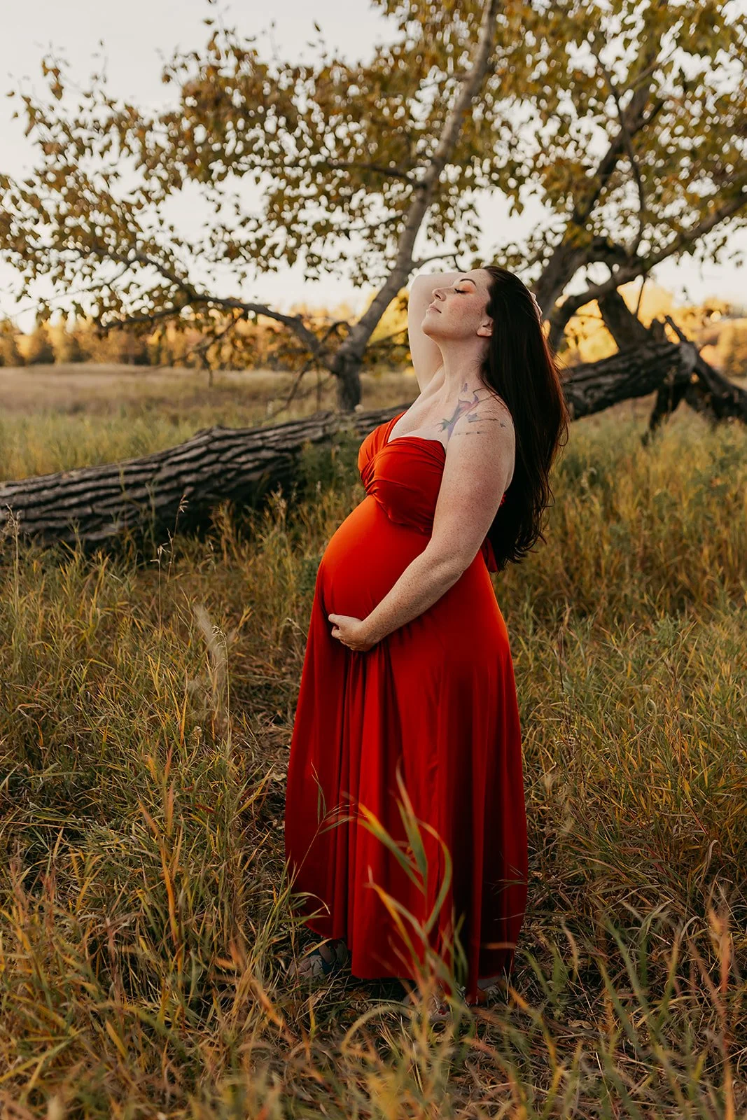 A pregnant woman wearing an orange red maternity infinity wrap dress in an autumn field outdoor photosession