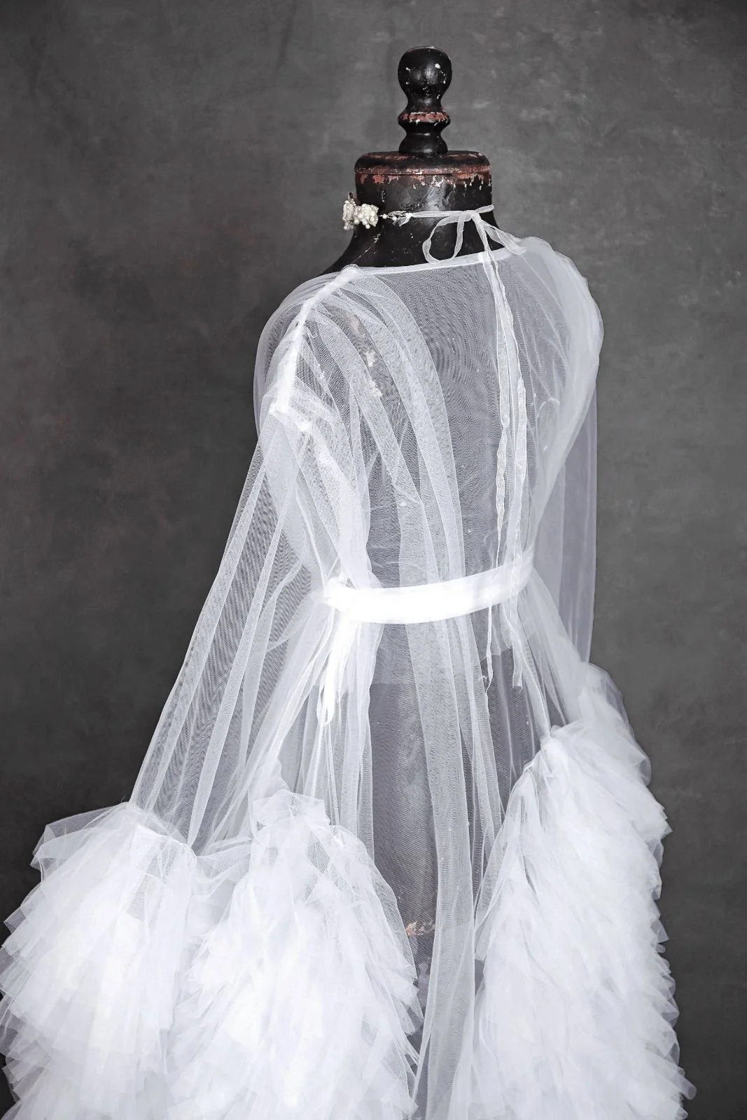 Back view of white sheer tulle floor-length robe with puffy textured sleeves, and jewellery ribbon
