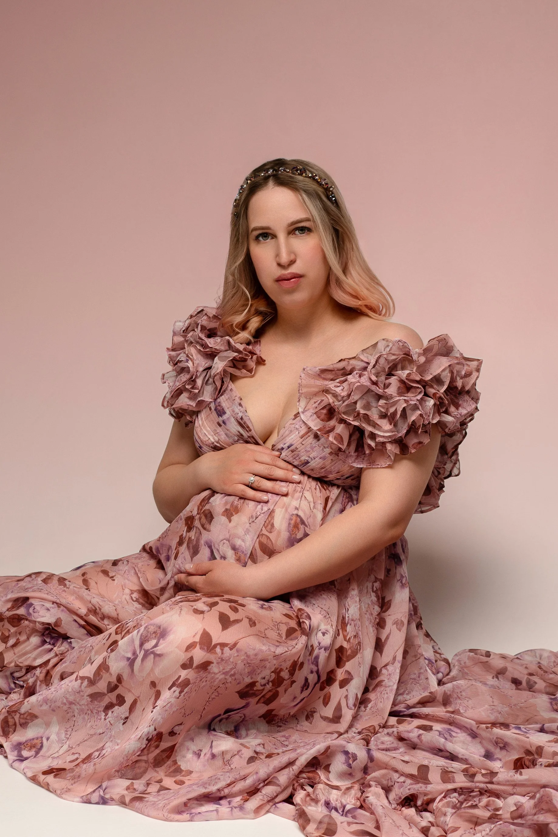 Portrait of a pregnant woman wearing a pink floral organza gown with off-the-shoulder v-neck corset, in a maternity photosession in Calgary