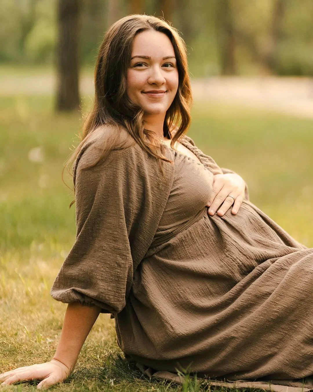 A pregnant woman wearing a khaki brown top and skirt dress, in an outdoor maternity photoshoot in Calgary