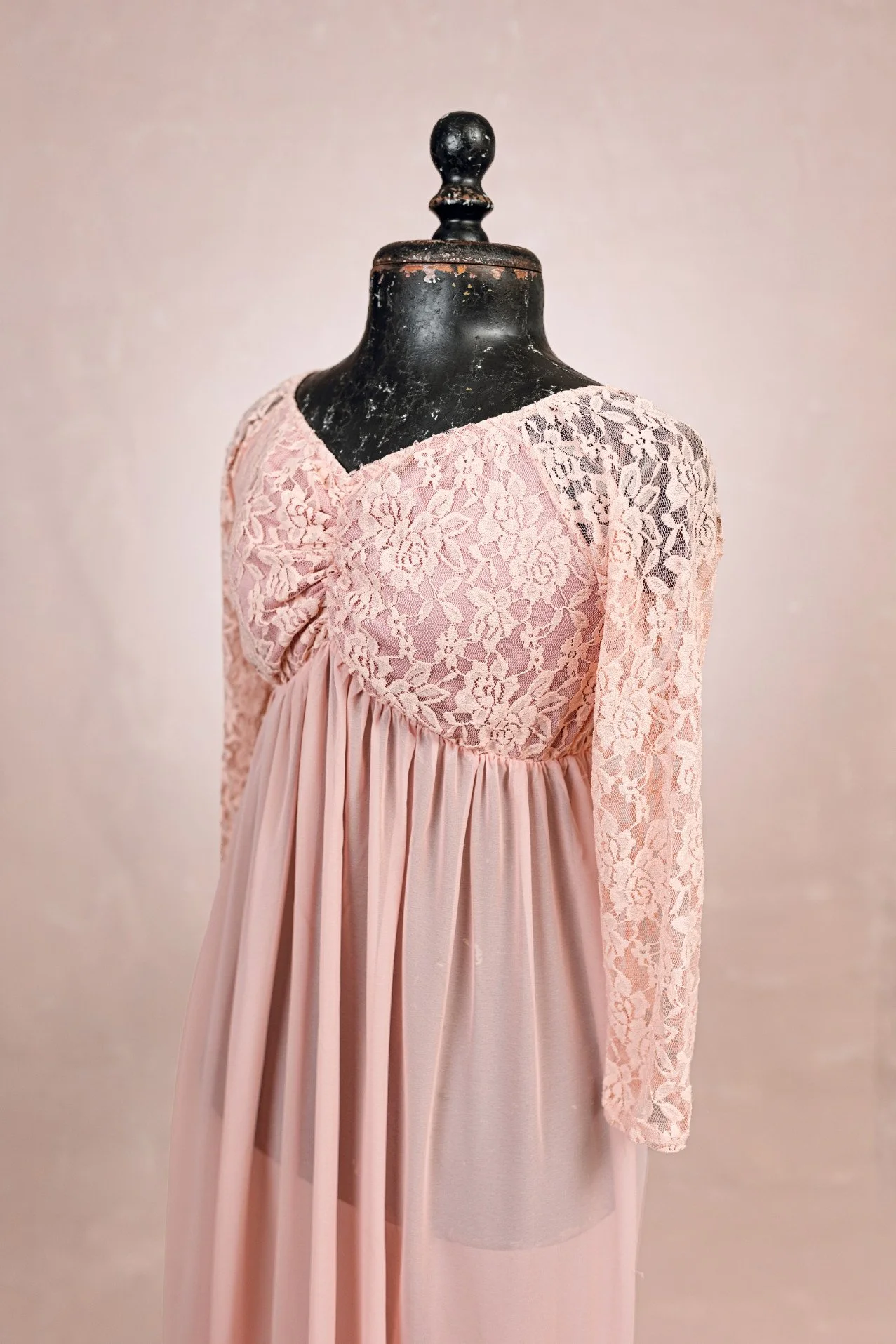 Close up of peach pink maternity photoshoot rental dress with translucent floor-length skirt, and lace upper with long sleeves