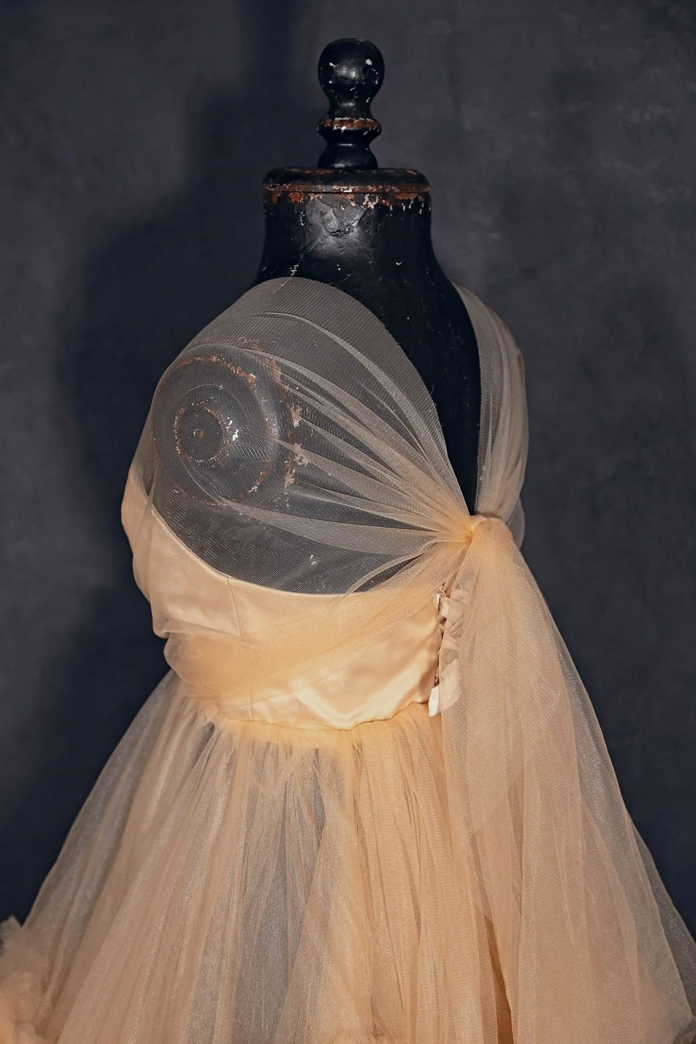 Closeup of a puffy tulle beige coloured gown on a mannequin. The skirt is layered tulle and the gown is shoulderless.