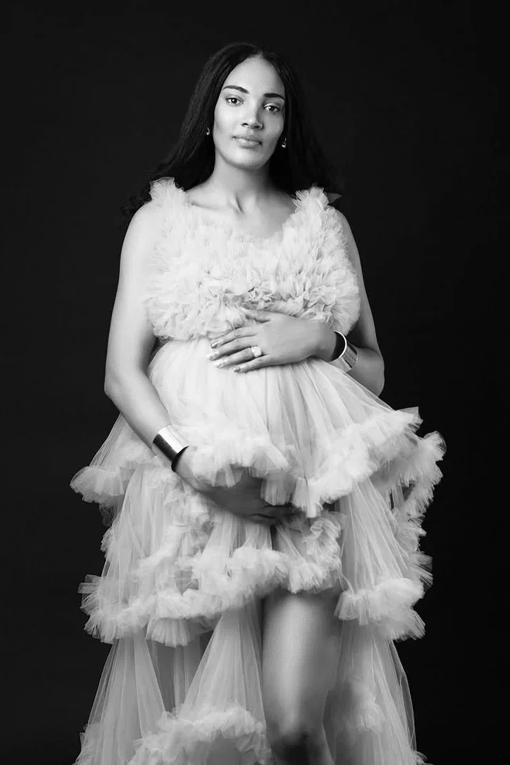 A pregnant woman wearing a beige coloured puffy tulle maternity gown in studio photoshoot