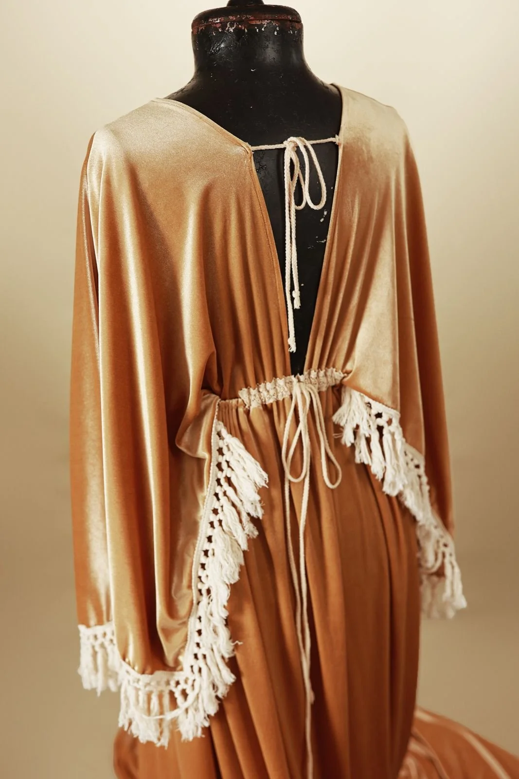 Back view of a golden yellow velvet gown with v-neck, open back, and long boho tassled sleeves