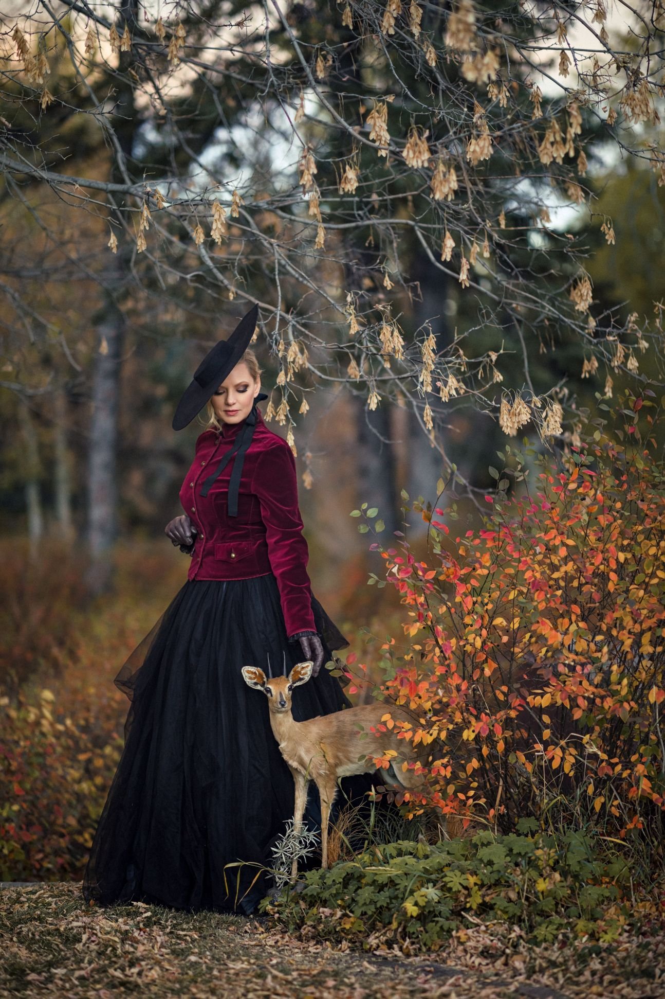 Woman wearing a black skirt and red velvet jacket in autumn Calgary park photoshoot