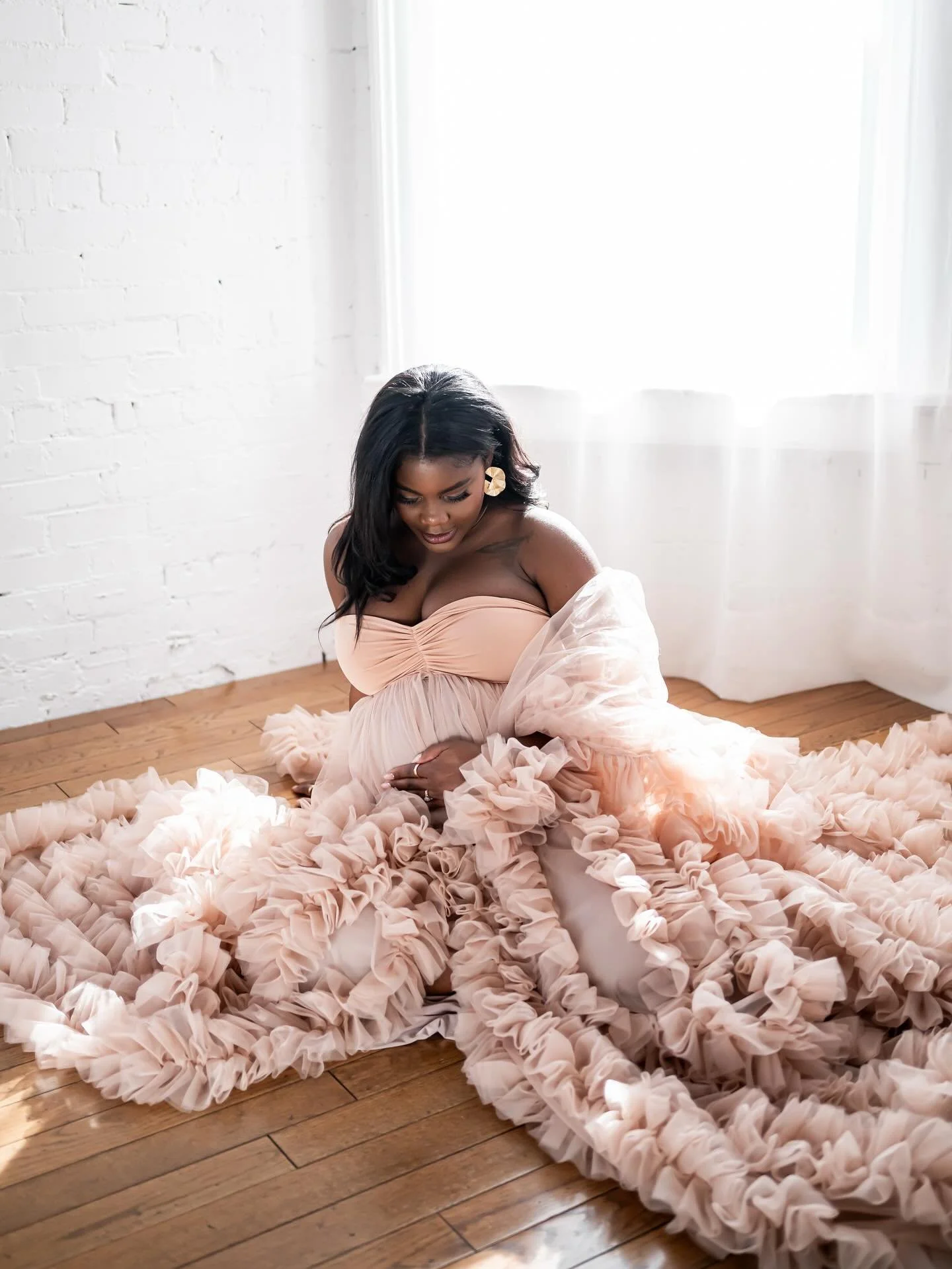 A pregnant woman wearing a ruffled tulle dusty rose gown, sitting on the floor