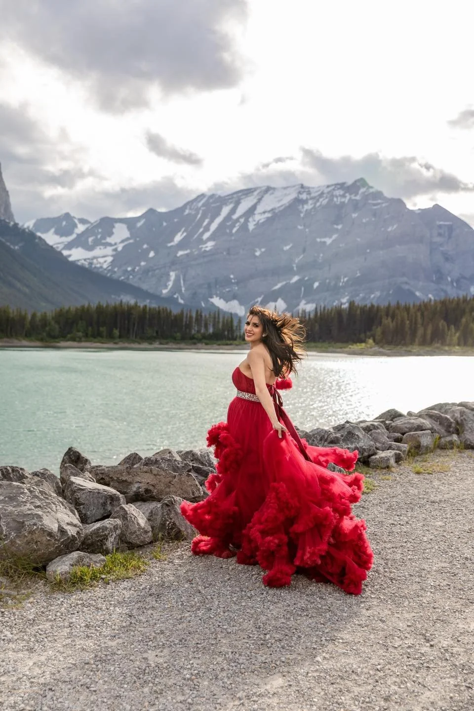 A woman wearing a red gown, standing in the mountains in an outdoor photoshoot in Calgary