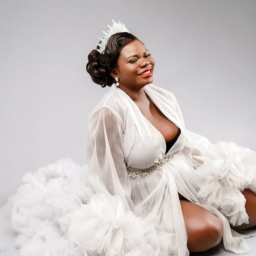 A pregnant woman wearing a white puffy sheer tulle gown in a studio maternity photoshoot setting