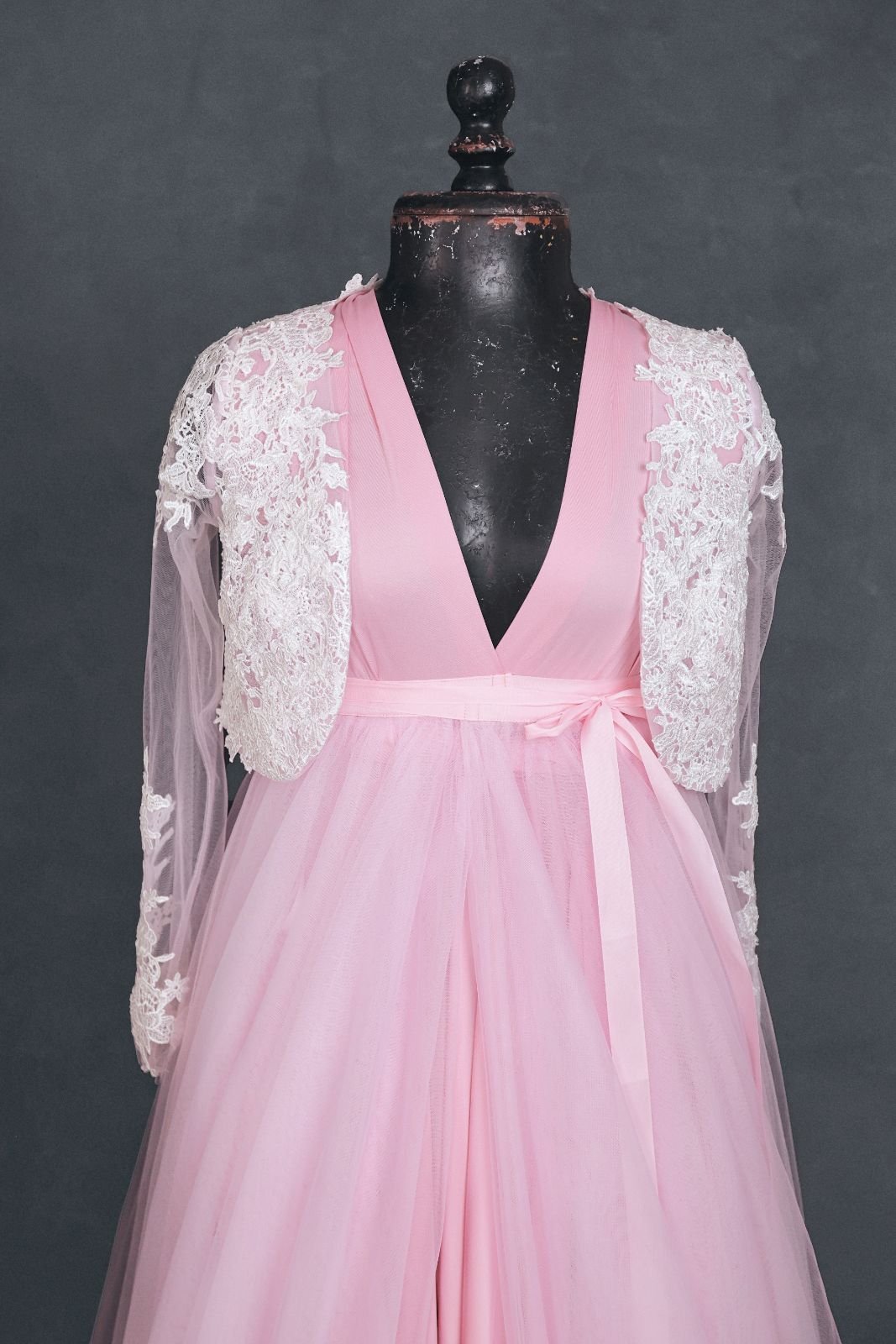 Close up of pink infinity dress with a tulle skirt and white lace coat added overtop, tied with a pink ribbon at the waist