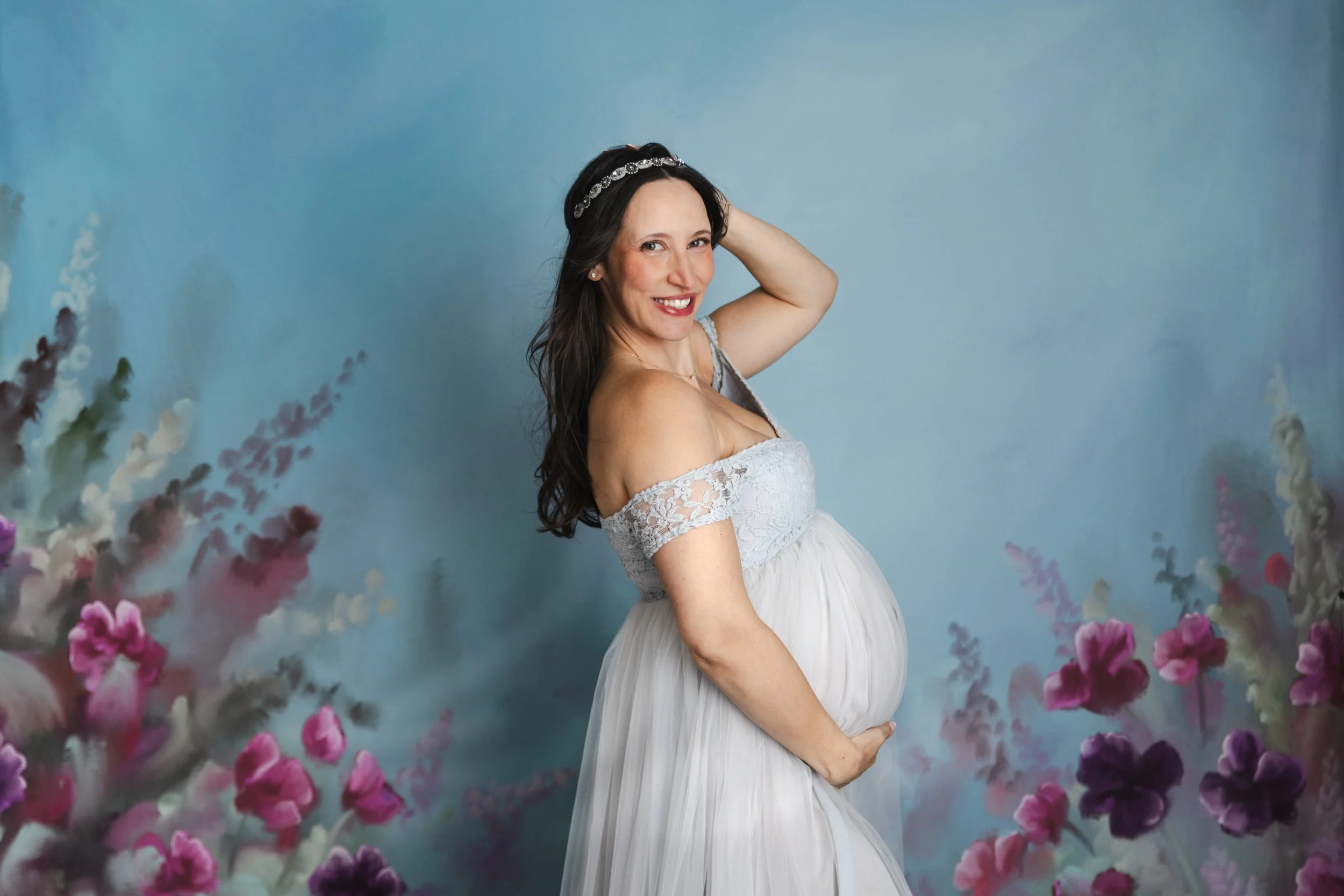 A pregnant woman wearing a silver tulle rental dress with off-the-shoulder embroidered corset, in a studio maternity photoshoot in Calgary