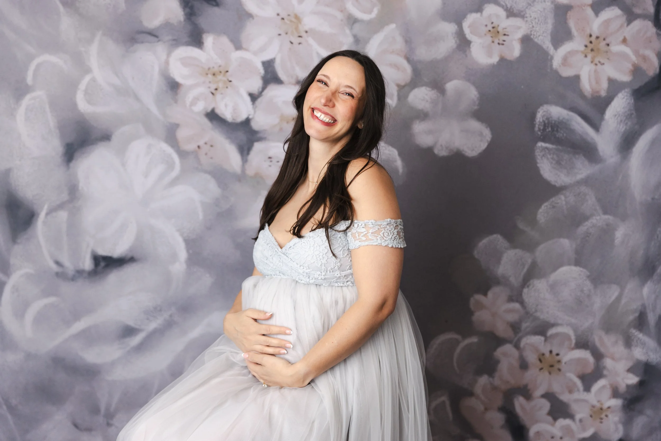 A pregnant woman wearing a silver tulle rental dress with off-the-shoulder embroidered corset, in a studio maternity photoshoot in Calgary