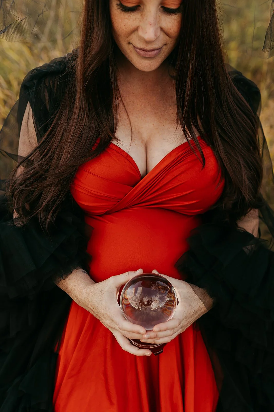 Close up of baby bump, of a pregnant woman wearing an orange infinity dress and black tulle ruffled robe