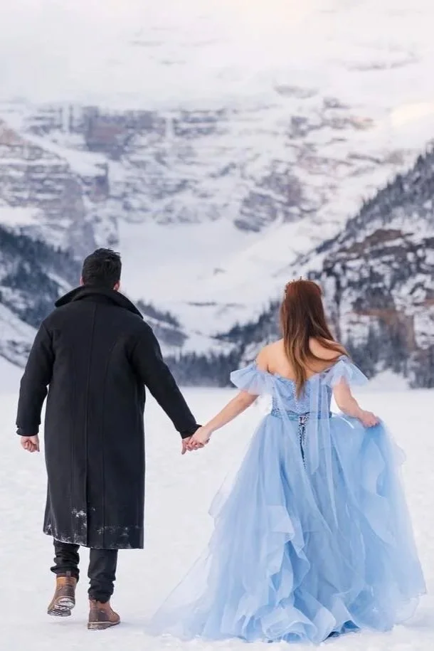 Bride and groom-to-be walking in Lake Louise, with bride wearing sky blue two-piece gown with embellished top