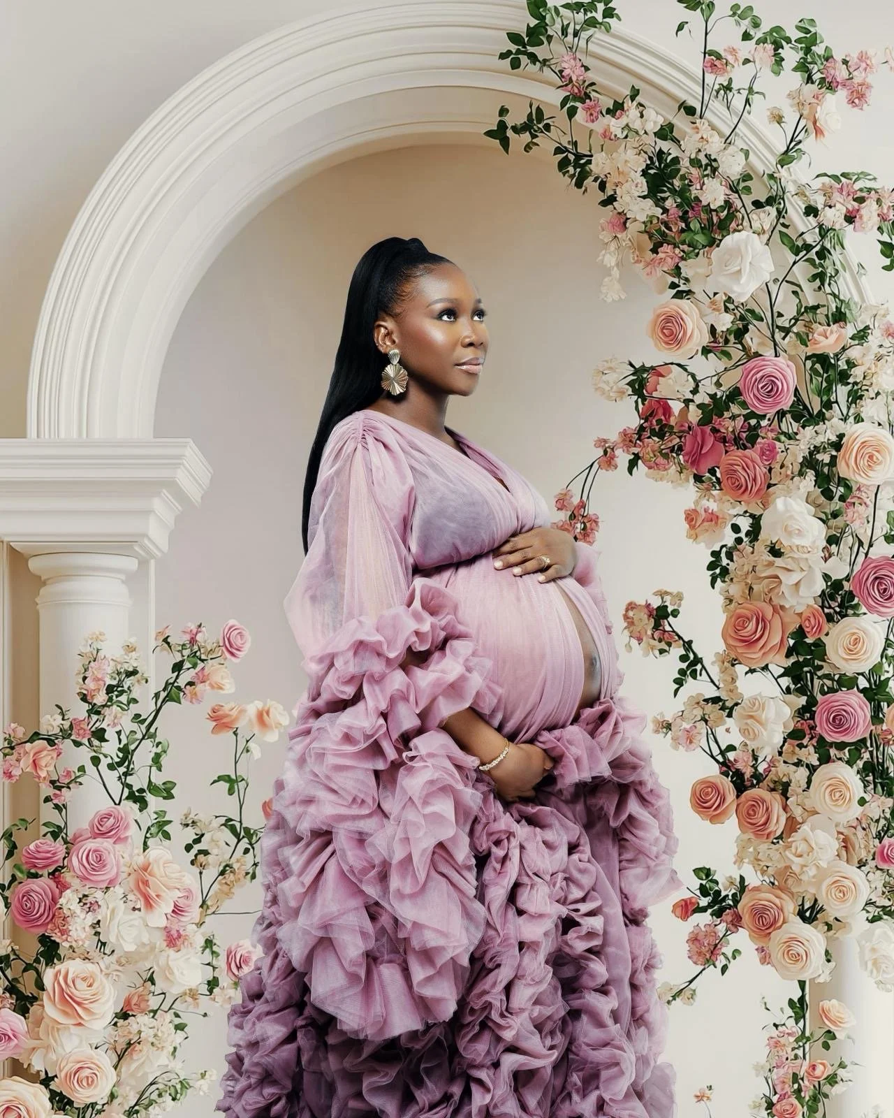Portrait shot of pregnant woman wearing a dusty pink maternity photoshoot robe with ruffles in studio photosession