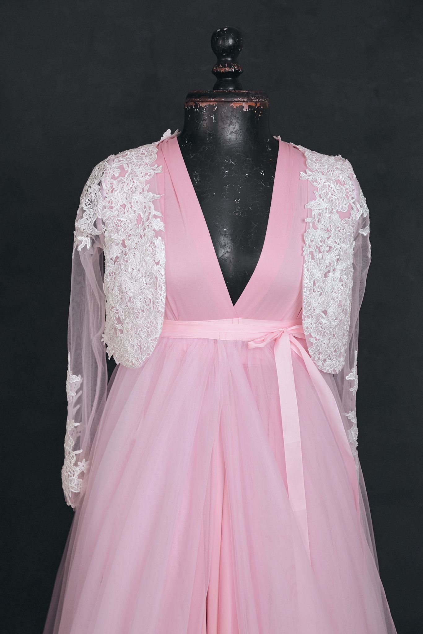 Close up of pink infinity dress with a tulle skirt and white lace coat added overtop, tied with a pink ribbon at the waist