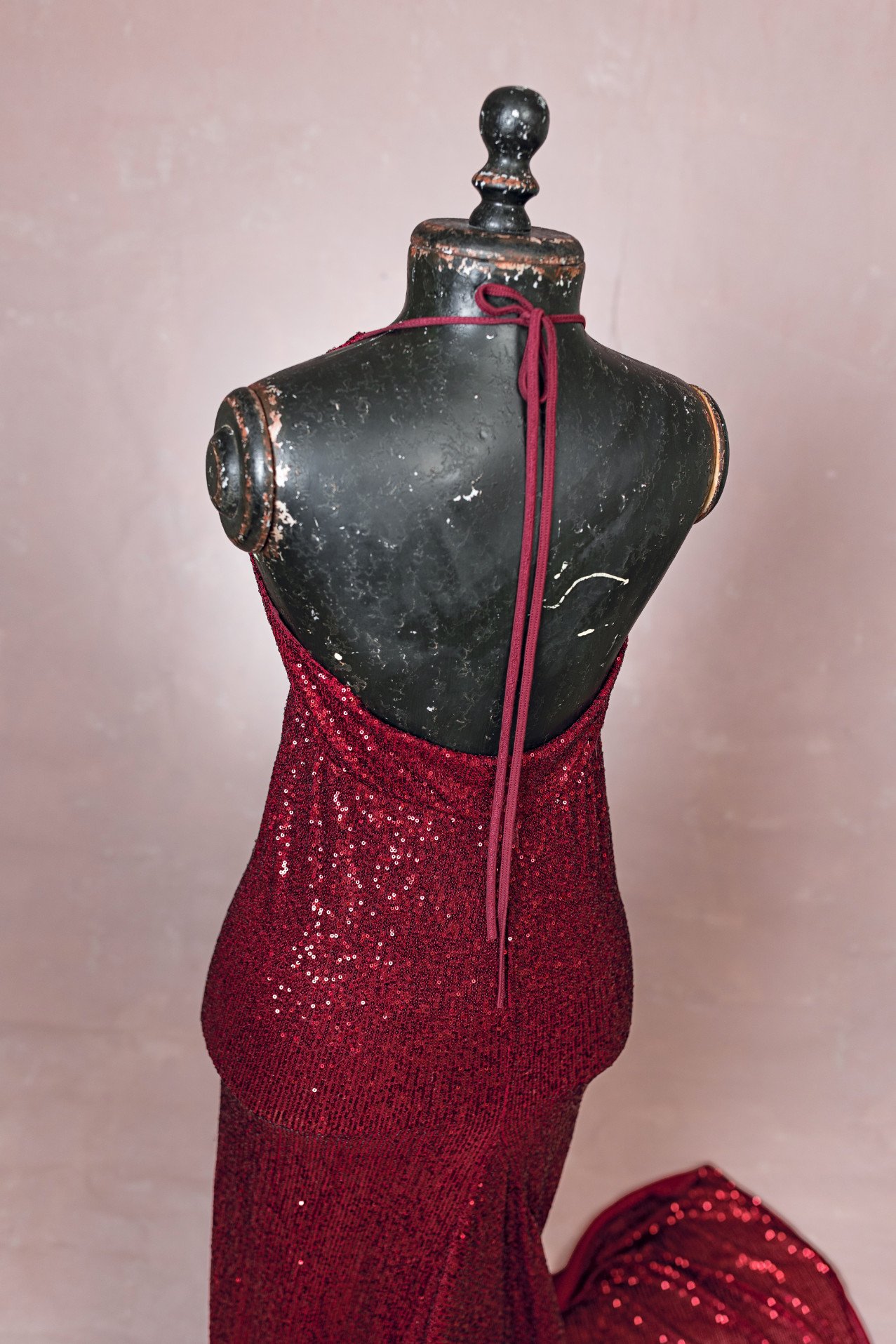 Back view of red sparkly sequin form-fitting designer gown, showing open halter stringtie back