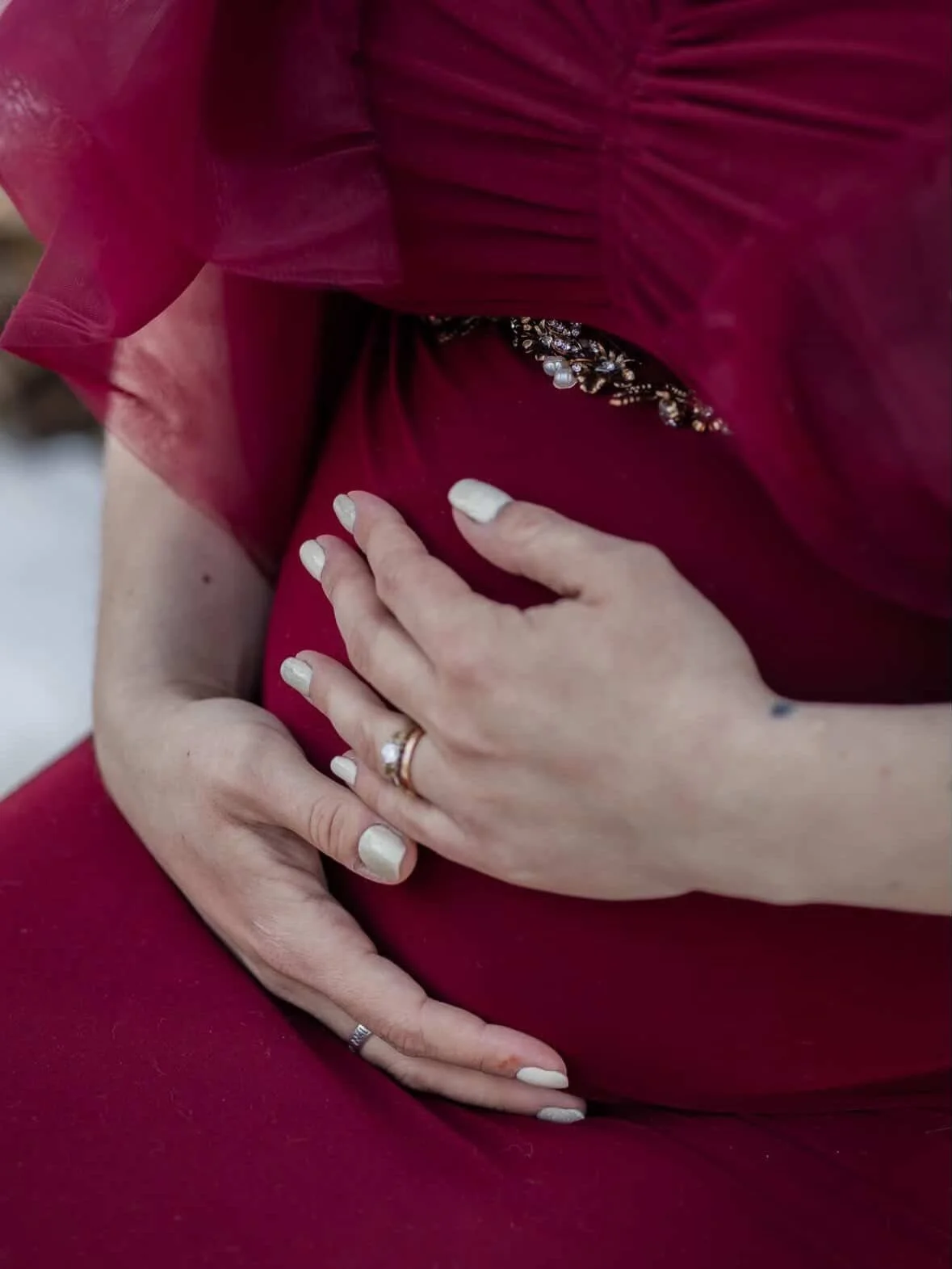 Close up of pregnant woman's baby bump, showing the red bodycon gown and tulle ruffles