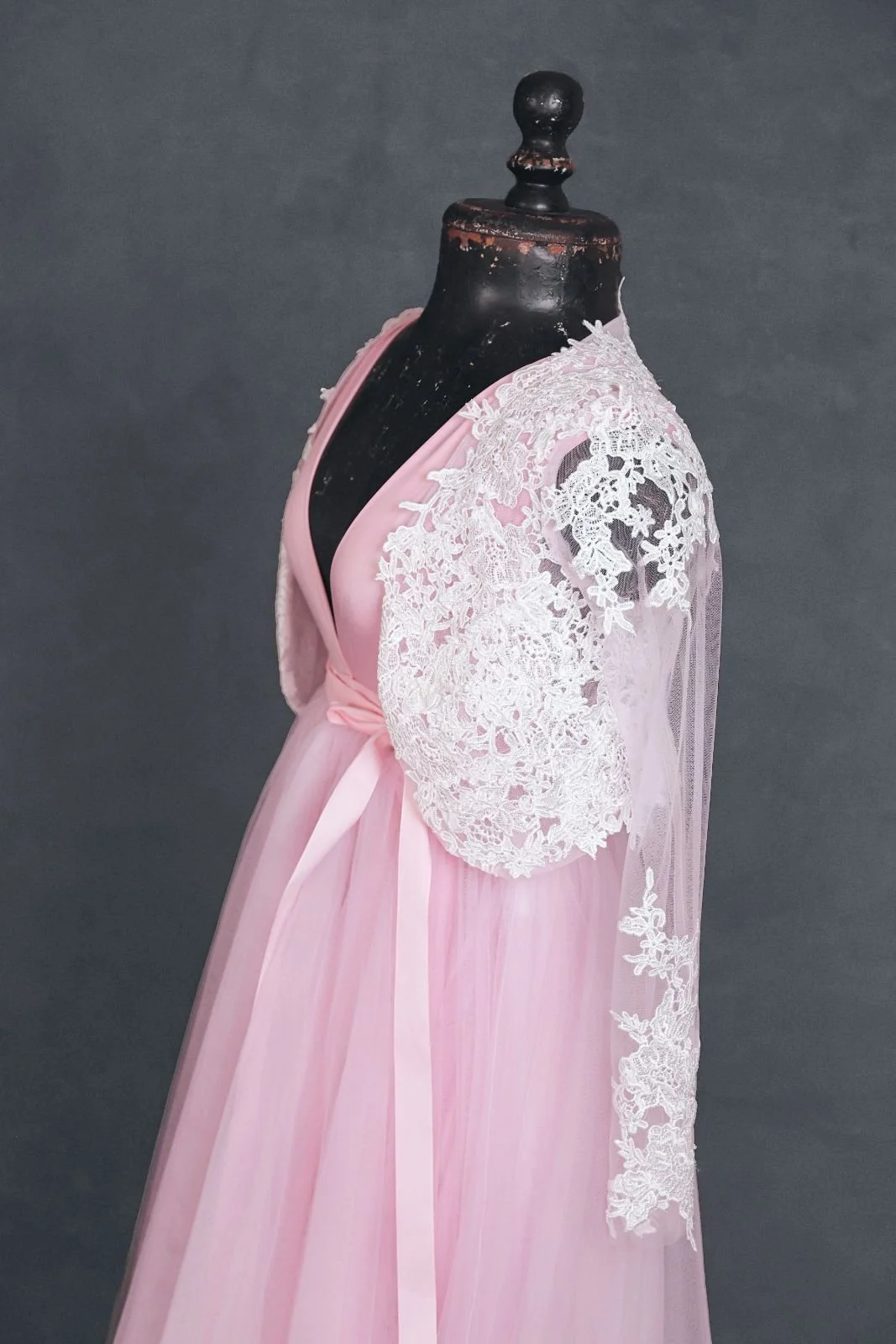Side view of pink infinity dress with a tulle skirt and white lace coat added overtop, tied with a pink ribbon at the waist