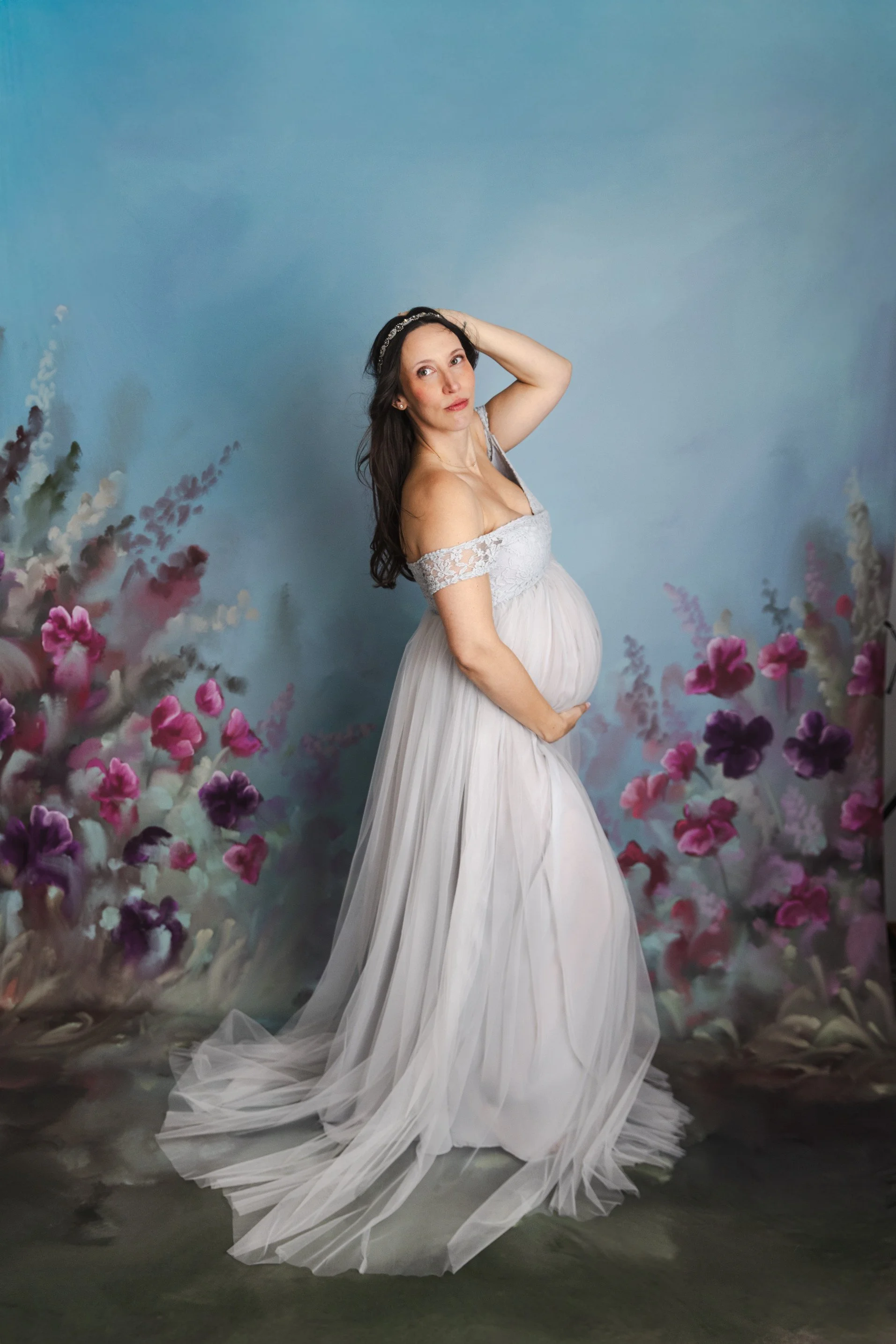A pregnant woman wearing a silver tulle rental dress with off-the-shoulder embroidered corset, in a studio maternity photoshoot in Calgary